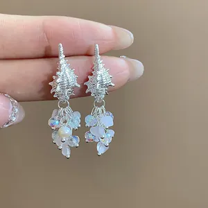 Macro view of silver conch shell stud earrings with crystal pearl bead tassels