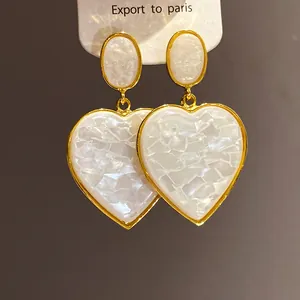 Detailed macro shot of vintage gold tone heart drop earrings with white shell mosaic pattern