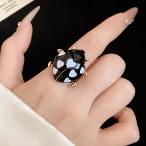 Detailed macro shot of a black ladybug ring with white heart patterns and gold finish