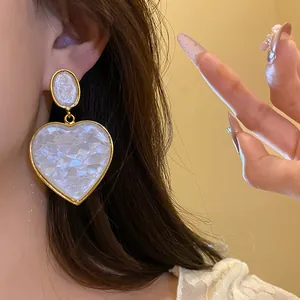 Close-up of a vintage white iridescent resin heart dangle earring worn on a model ear