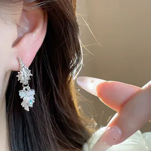 Close-up of shell-shaped earrings with pearl tassels worn on a woman's ear.