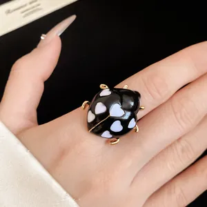 Detailed macro shot of a black ladybug enamel ring with white heart patterns on finger