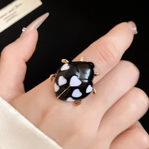 Close-up detail of black enamel ladybug open ring with white heart spots design