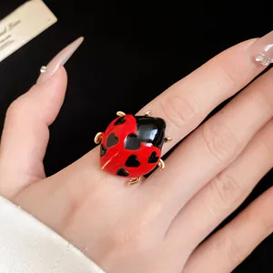 Close-up detail of a ladybug ring with red enamel and black heart spots on a finger.