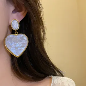 Detailed close-up shot of elegant vintage white resin heart dangle earrings on model