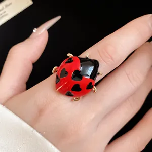 Detailed view of an enamel ladybug ring with black heart patterns on a red shell.