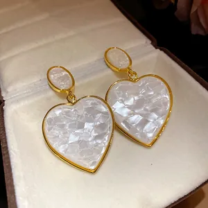 Detailed view of vintage gold-toned heart drop earrings with white textured resin inlay
