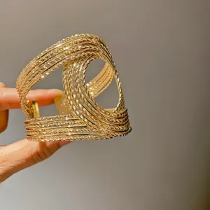 Detailed close-up of a gold-toned metal cross hollow open bracelet with woven texture
