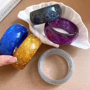 Close-up of vibrant resin bangles featuring glitter stars and snowflakes on a shell tray
