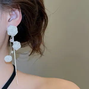 Side view detail of elegant mesh rose earrings with long silver tassels on a model's ear.