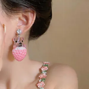 Vista detallada de pendientes de resina rosa con oso y fresa en una modelo