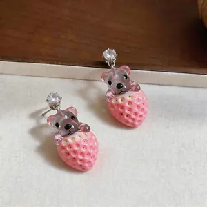 Primer plano de lindos pendientes de resina con osito y fresa y circonitas brillantes