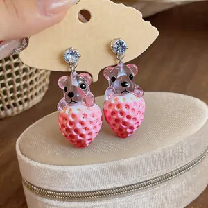 Vista de detalle de pendientes de oso y fresa de resina con circonitas brillantes.