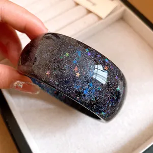 Detailed close-up of a black resin bangle with colorful star glitter and starry sky effect.