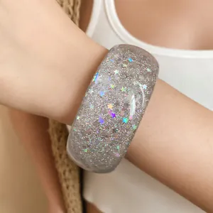 Macro view of a wide resin bangle featuring iridescent star patterns and glitter on a wrist