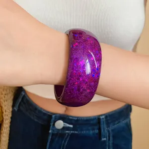 Close-up of a chunky purple resin bangle with glitter and star inclusions on a wrist