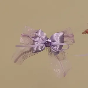 Dettaglio di un fermaglio per capelli con fiocco in pizzo viola e gemma centrale