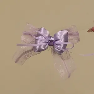 Primo piano di un fermaglio per capelli a fiocco in raso e pizzo viola con gemma