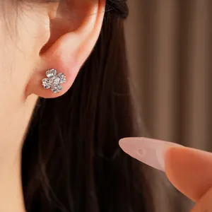 Close-up detail of minimalist clover flower stud earrings with sparkling zircon stones worn