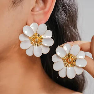 Detailed view of oversized white enamel flower stud earrings with a gold center
