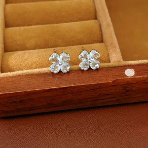 Close-up of light blue zircon clover stud earrings presented in a wooden jewelry box.