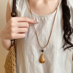Détail rapproché d'un collier avec pendentif en goutte tissé à la main et perle bois.