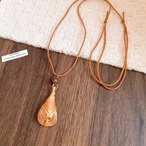 Détail d'un collier pendentif goutte tissé à la main avec perle en bois et cordon marron