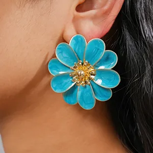 Close-up of a blue enamel flower earring on an ear with golden details