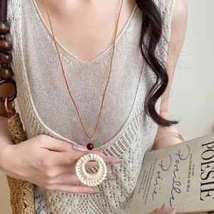 Gros plan d'un collier pendentif en rotin tressé bohème avec perle rouge et cordon