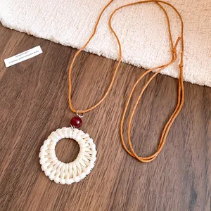 Vue détaillée d'un pendentif circulaire en rotin tressé avec perle en bois sur cordon tan