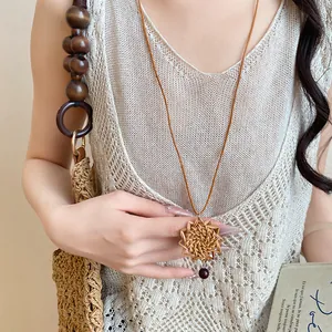 Détail d'un collier bohème avec pendentif fleur en rotin tressé sur robe en tricot
