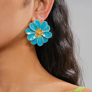 Close-up view of vibrant blue enamel flower stud earrings worn by a fashion model