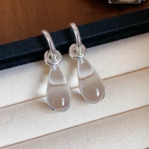 Macro detail of elegant silver-tone C-shape hoop earrings with clear resin teardrops