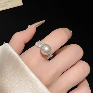 Detailed close-up view of a luxury zircon and pearl open ring on a female finger.