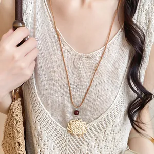 Gros plan d'un collier bohème avec pendentif fleur en paille tressée et perle bois.