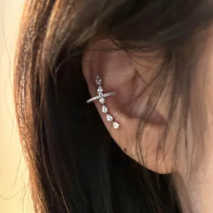 Macro view of a silver cross ear cuff decorated with cubic zirconia on a female model's ear