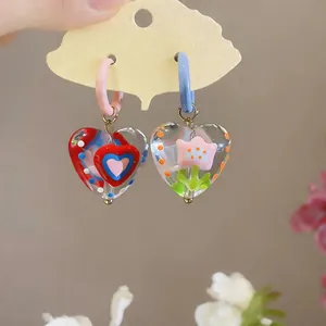 Detailed view of sweet-style glazed glass heart earrings with floral and heart motifs