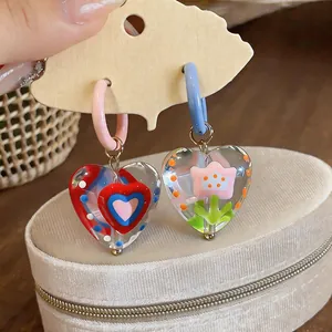 Close-up detail of colorful glass heart earrings with floral and polka dot patterns