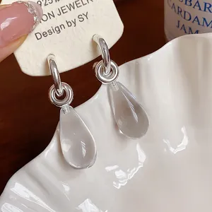 Close-up view of elegant clear resin teardrop earrings with minimalist silver C-shape hoops.