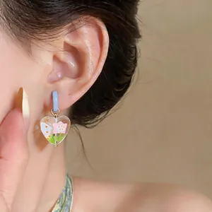 Close-up of sweet heart-shaped glass earring with pink flower motif worn on ear.