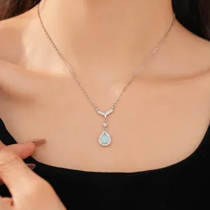 Silver necklace featuring a zircon-encrusted fish tail and blue teardrop pendant on a model