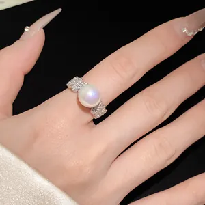 Detailed macro view of an elegant pearl ring with pavé-set zircons on a finger.