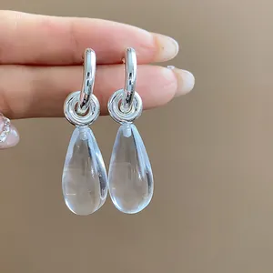 Close-up of silver C-shaped hoop earrings with clear resin teardrop charms.