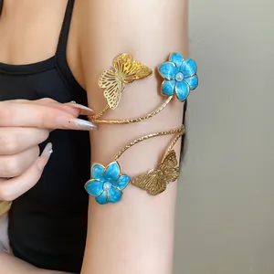 Detailed view of a gold-toned metal butterfly and blue enamel flower arm cuff on a model's arm