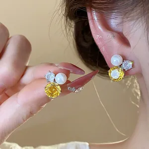 Close-up of elegant flower stud earrings with yellow zircon and white pearl detail
