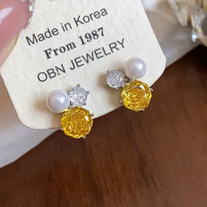 Close-up detail showing exquisite yellow flower zircon and white pearl stud earrings on card.