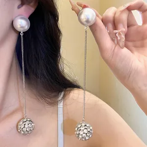 Close-up detail of long silver dangle earrings with a large pearl and rhinestone ball.