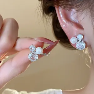 Close-up of exquisite silver needle earrings with shimmering zircons and a white pearl.