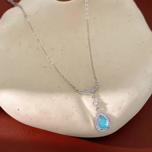Close-up detail of silver necklace featuring a blue teardrop pendant and zircon fishtail
