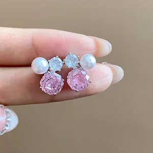 Macro detail view of pink flower zircon and pearl earrings held on delicate fingertips.